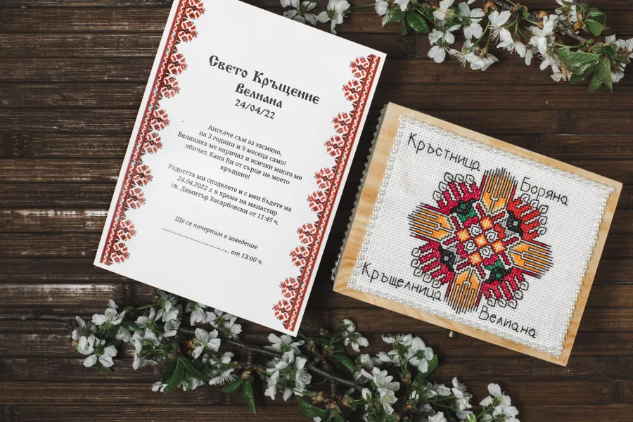 A christening invitation with embroidery motifs and a wooden box with a cross-stitched lid